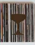 A square shaped book with photograph of vinyl stack for cover with gold coctail glass on top. Text on book reads, "Booze and Vinyl. Photographed on white background. 