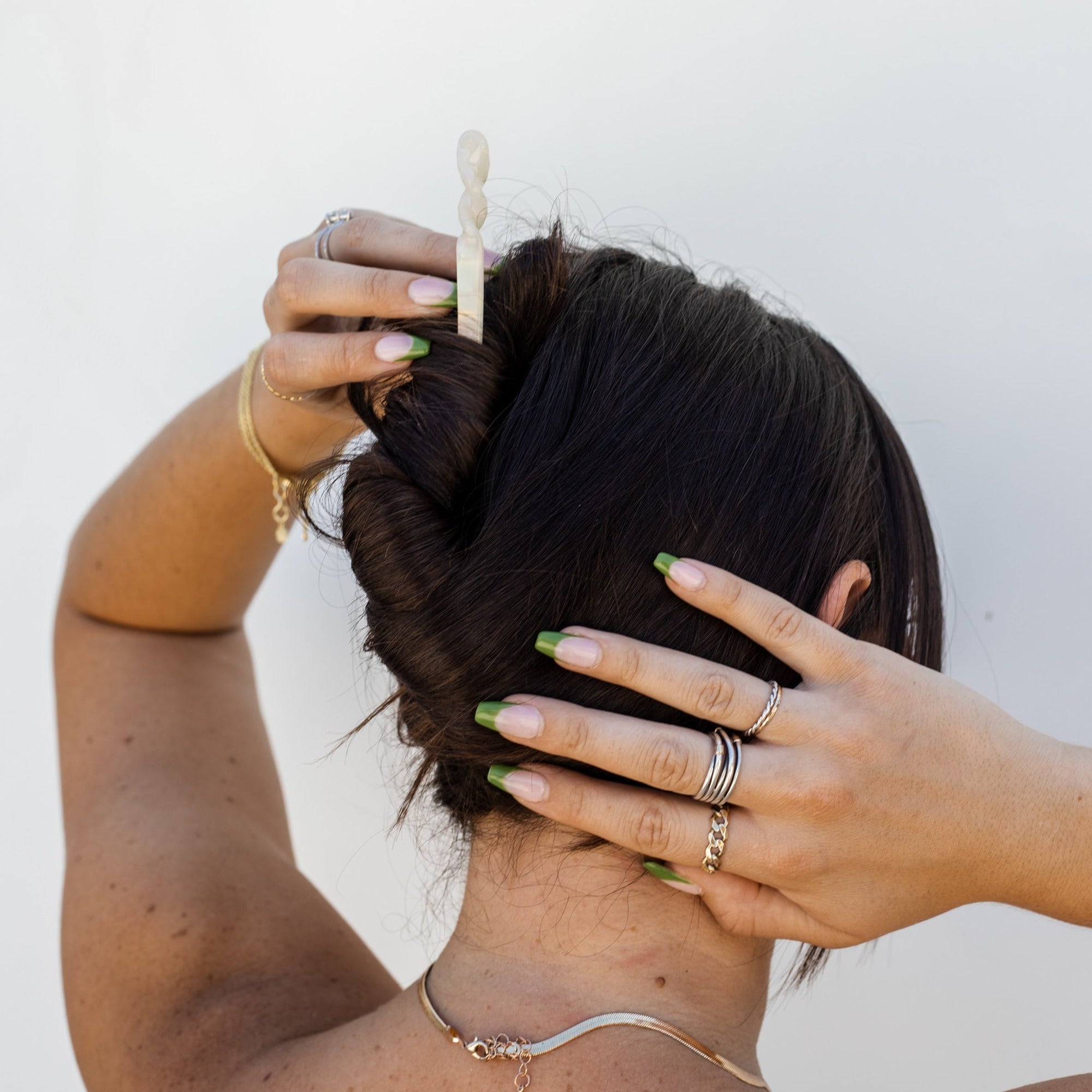 Girl with dark brown hair wearing a twisted updo with a white marble hair stick against a white wall background