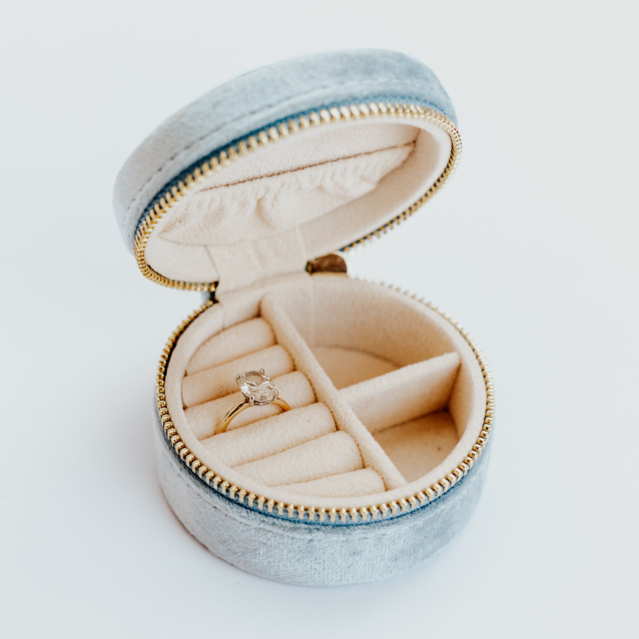 Light blue velvet jewelry travel case holding an oval engagement ring against a white background