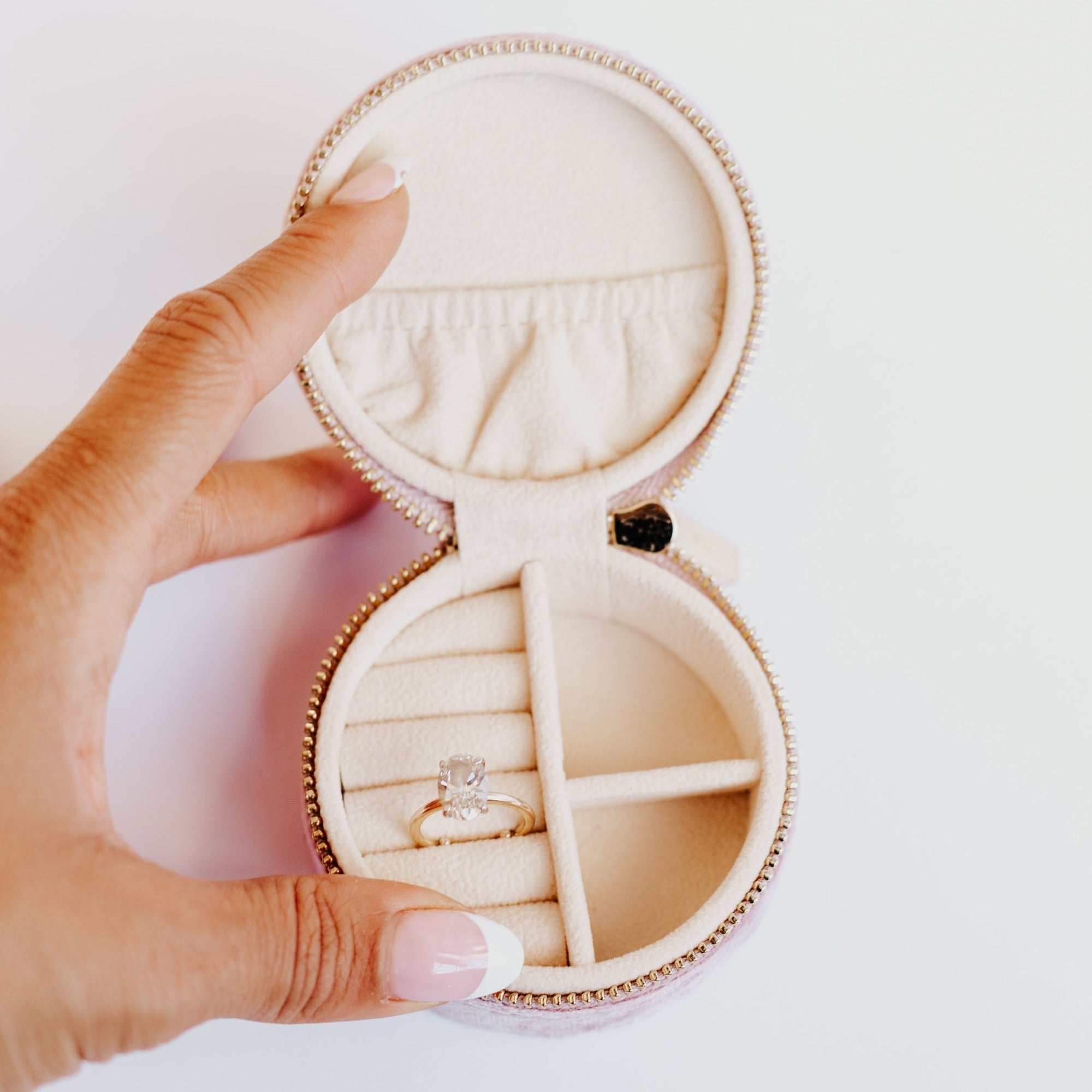 Light pink velvet jewelry travel case holding an oval engagement ring against a white background