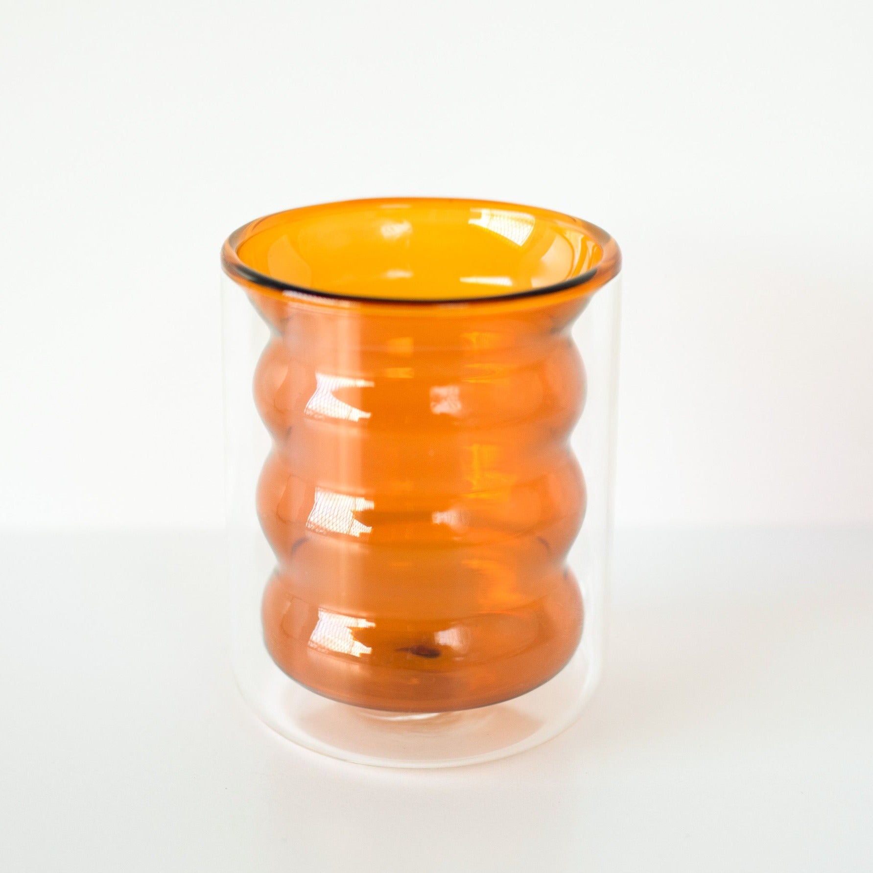 A double-walled amber orange rippled glass standing upright shot against a white background.