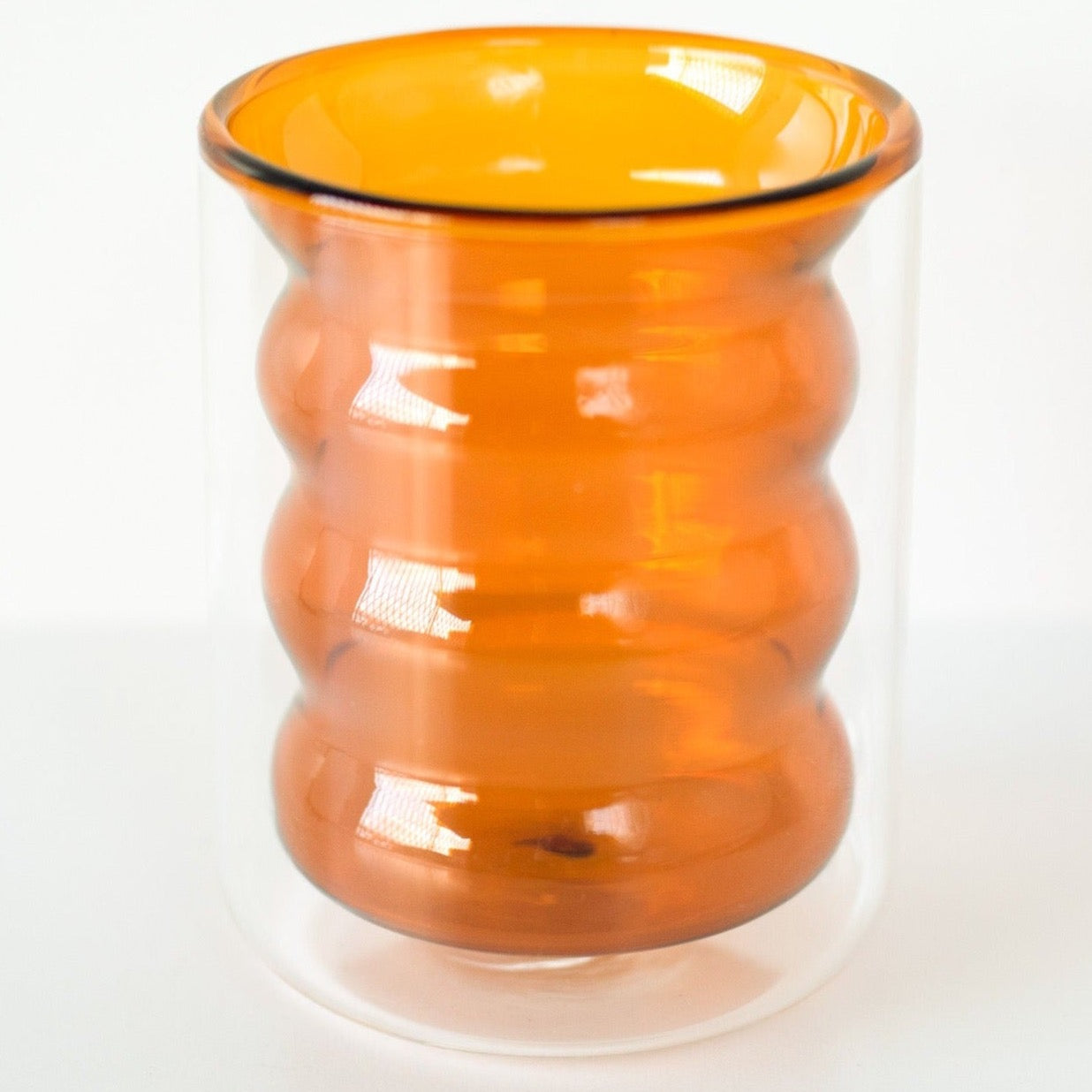 A double-walled amber orange rippled glass standing upright shot against a white background.