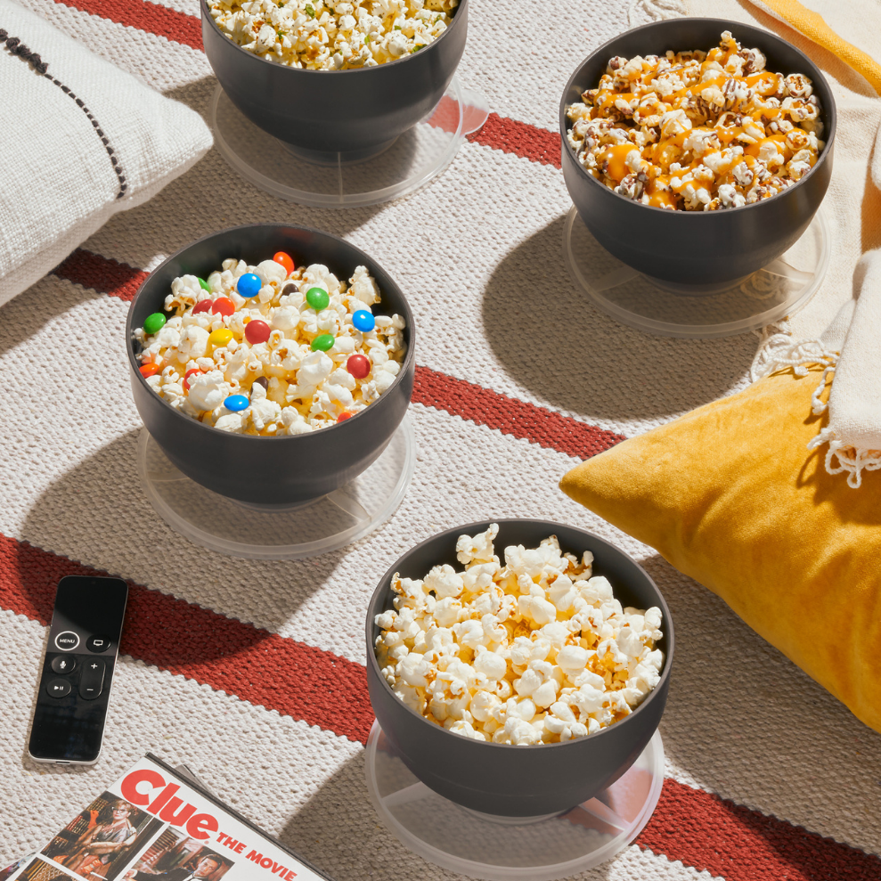 4 bowls of gourmet popcorn spread out with pillows and movies on the floor.