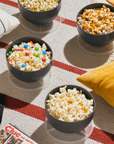 4 bowls of gourmet popcorn spread out with pillows and movies on the floor.