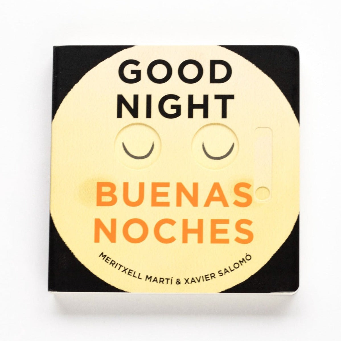 A black board book with yellow moon with closed eyes on front. Text on book reads, "Good Night Buenas Noches Meritxell Marti & Xavier Salomo". Photographed on white background.