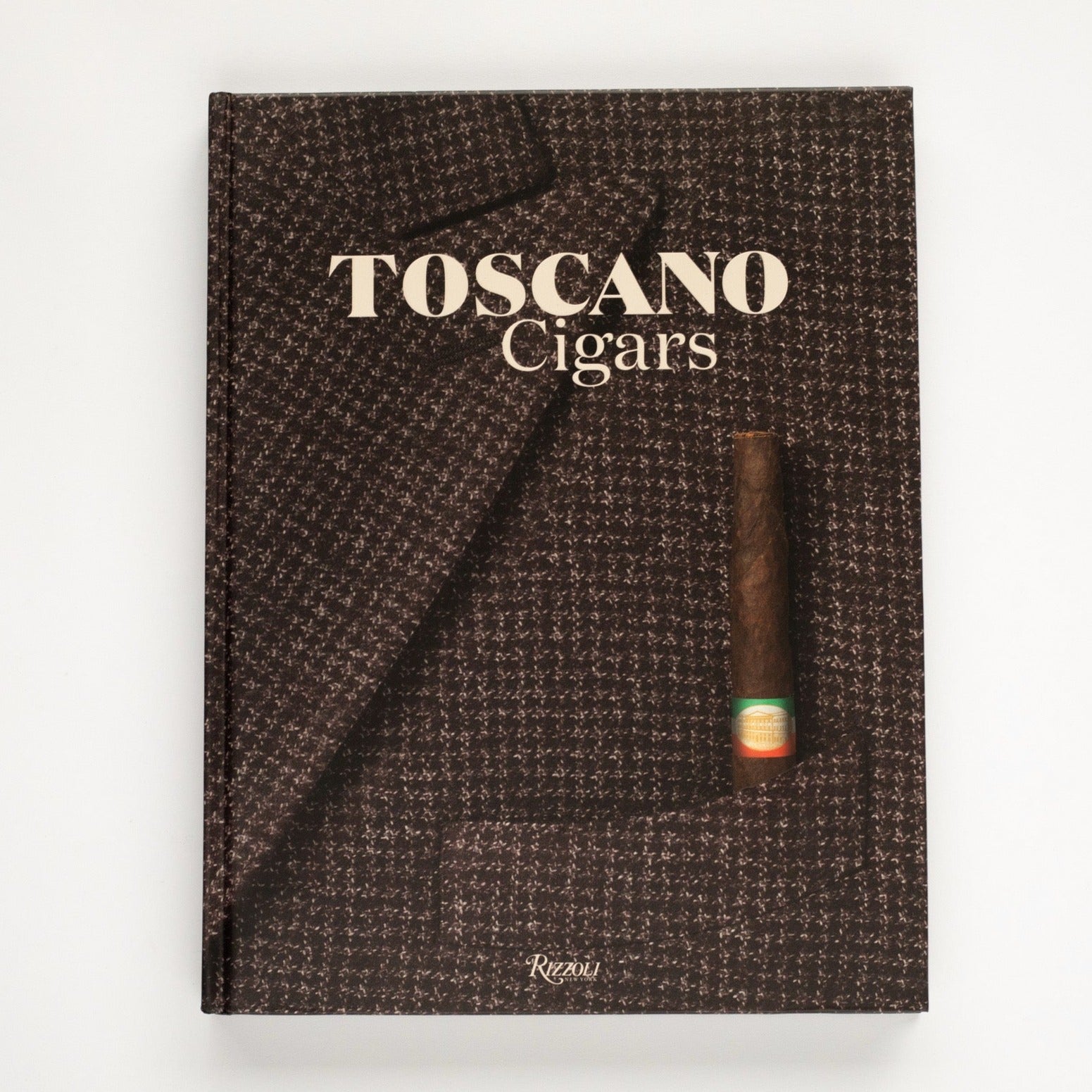 The front cover of "Toscano Cigars" photographed on a white background. The cover is a close up of a men's brown tweed suite jacket with a brown cigar sticking out of the chest pocket.