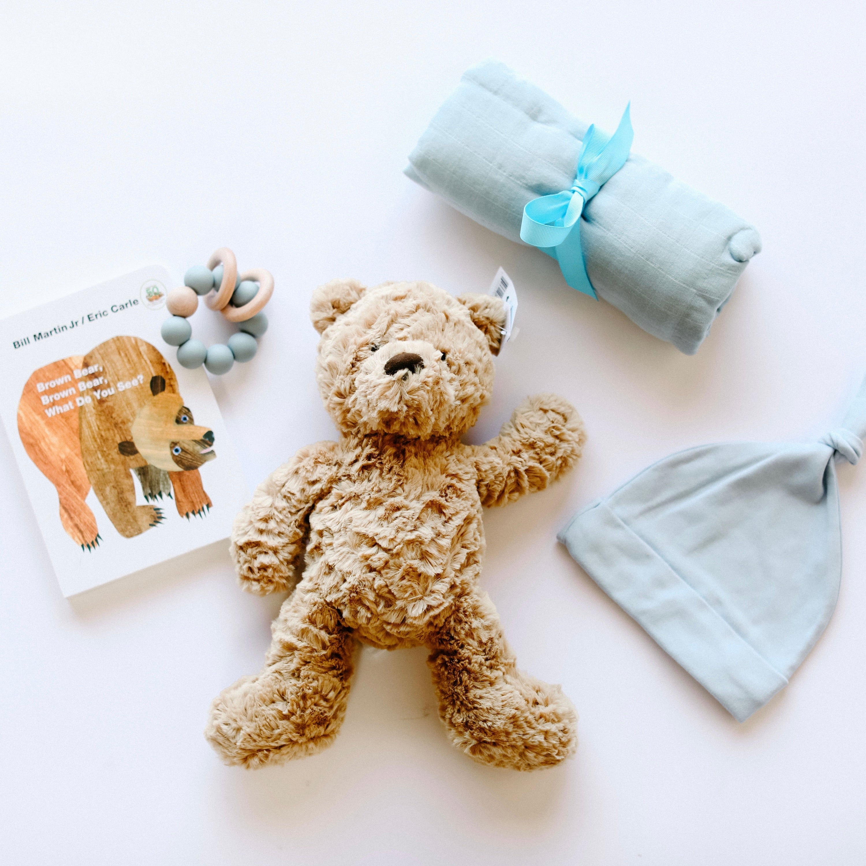 "Brown Bear, Brown Bear" Board Book, Alva Blue Knotted Baby Beanie, Alva Blue Wood Teething Ring, Alva Blue Swaddle and Jelly Cat Bumble Bear on white background.