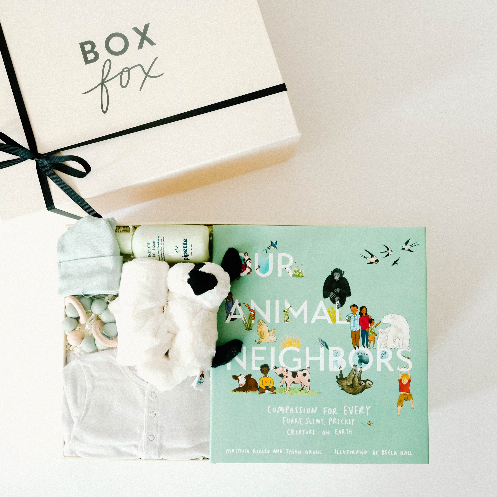 BOXFOX Original creme New Family Gift Box packed with PEHR cozy grey kimono onesie 3-6 months, Jellycat puppy lovey, Our Animal Neighbors book, Pipette baby oil, Alva sage green teether, and Alva sage green beanie.