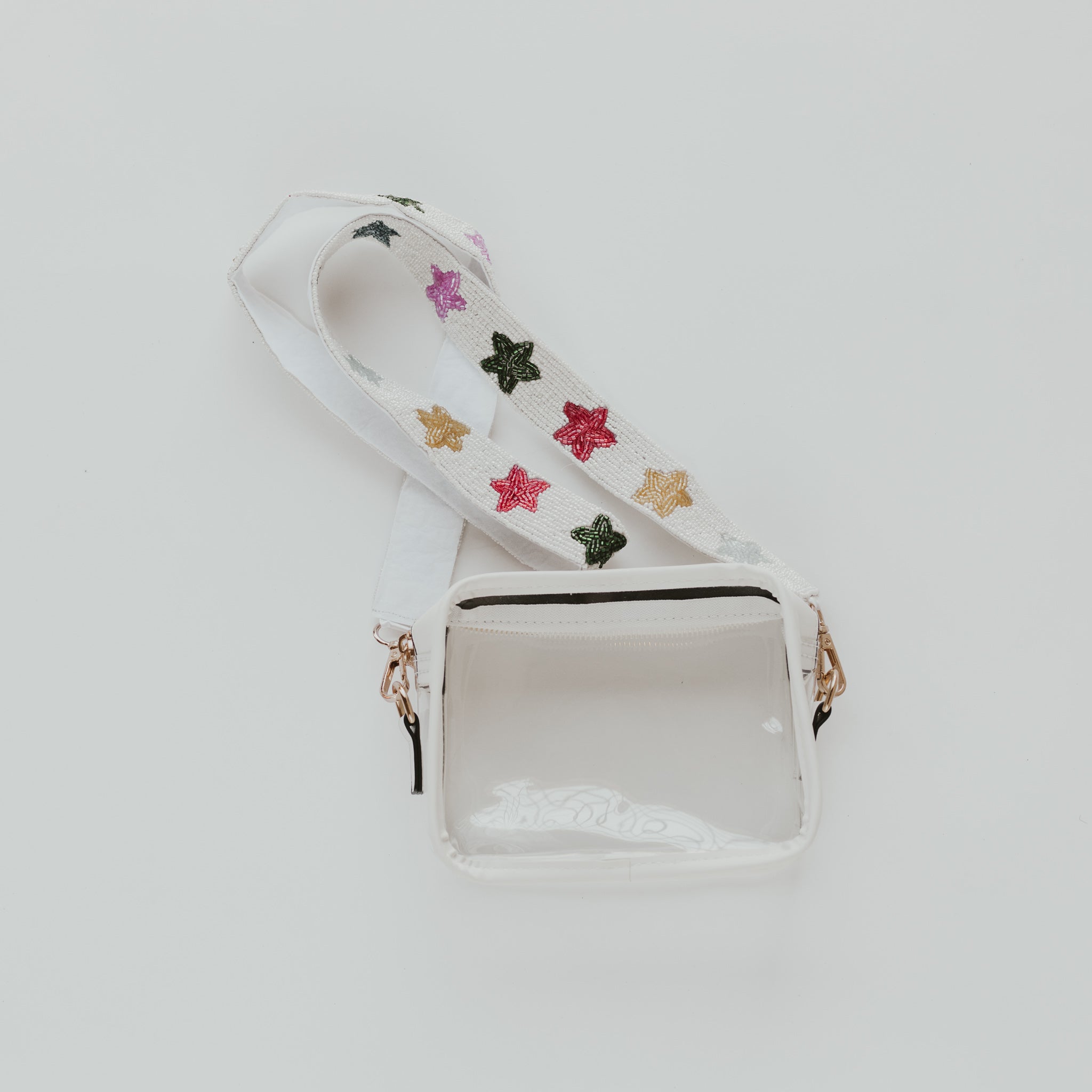A clear purse with white lining and a white beaded bag strap with rainbow beaded stars along the length of the strap against a white background