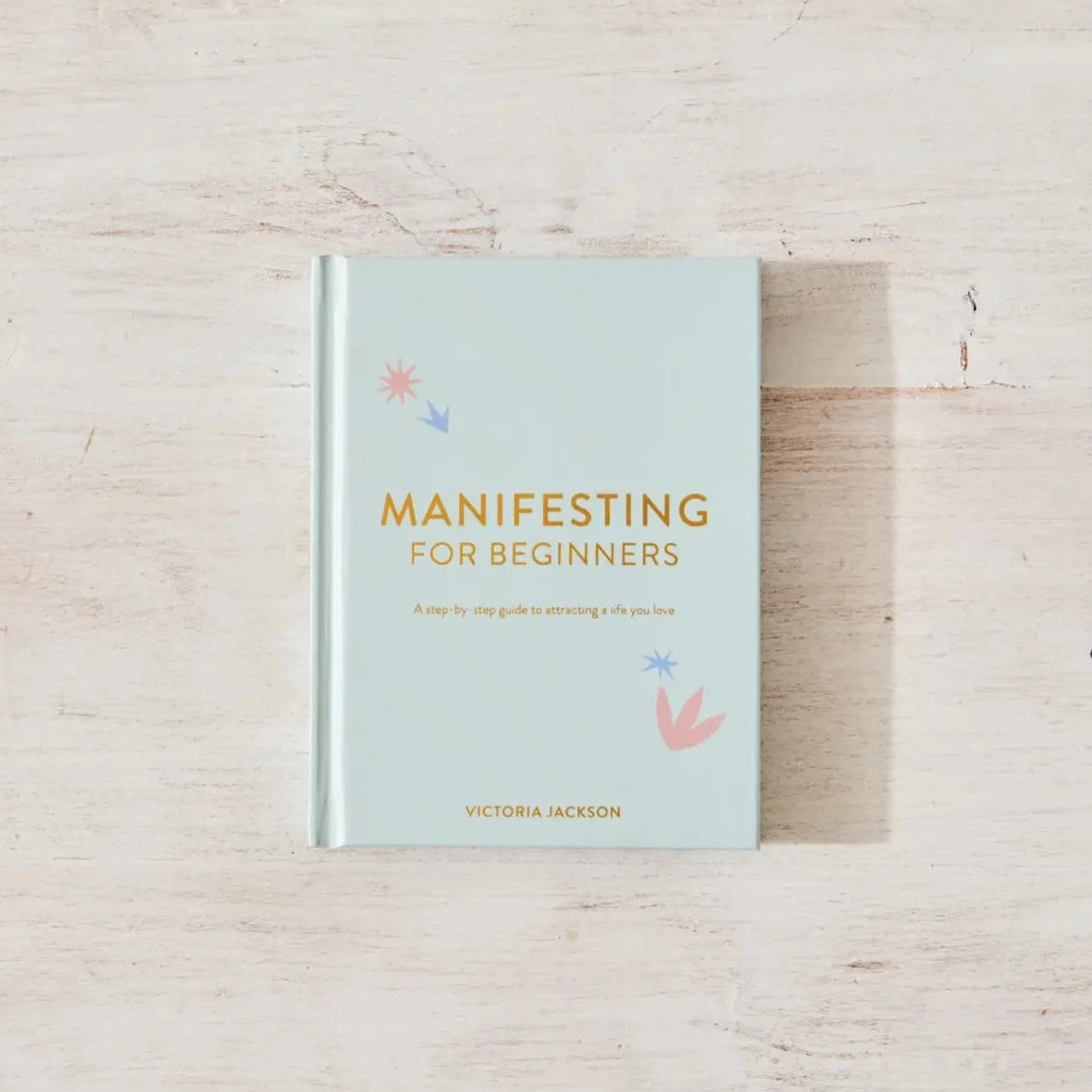 Light blue cover with dark yellow text that reads &quot;Manifesting for beginners&quot;. Has small pastel pink and blue illustrations on the top left and bottom right of the cover text
