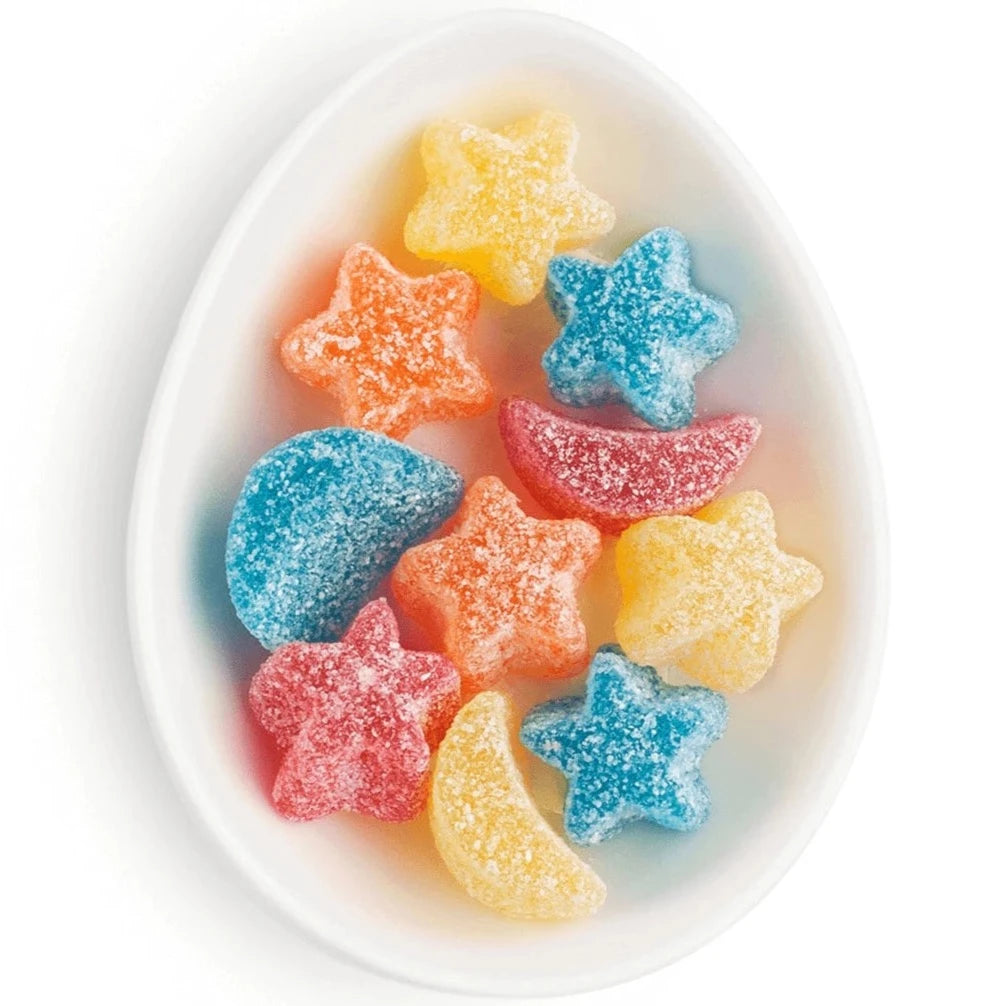 Star and moon shaped sour gummies in varying colors like blue, yellow, orange, and red. Candy's are in an oval white dish