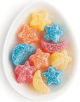 Star and moon shaped sour gummies in varying colors like blue, yellow, orange, and red. Candy's are in an oval white dish