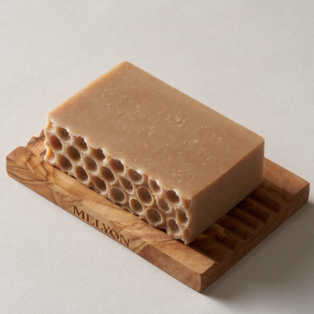 light brown soap with holes imprinted on the top. soap is resting on wooden soap holder